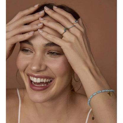 Woman smiling, wearing blue bracelet and rings, showcasing jewelry accessories.
