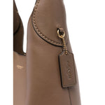 Close-up of light brown leather Coach Brooklyn leather hobo bag showing logo plaque and pendant detail.