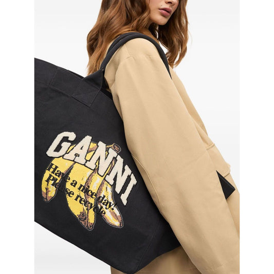 Woman holding Ganni Organic cotton XXL tote bag with black graphic print and logo on front.